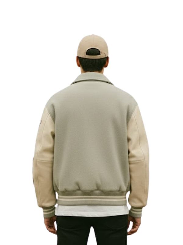 Person wearing a beige varsity jacket with leather sleeves on a white background