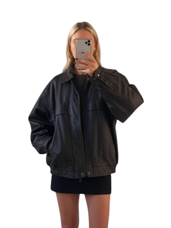 Person wearing a black jacket taking a mirror selfie on a white background