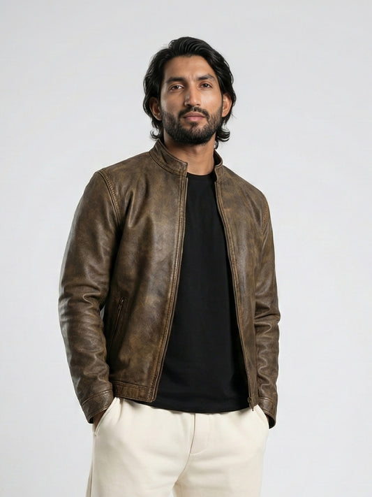 Man wearing a brown leather jacket over a black shirt with white pants on a light gray background