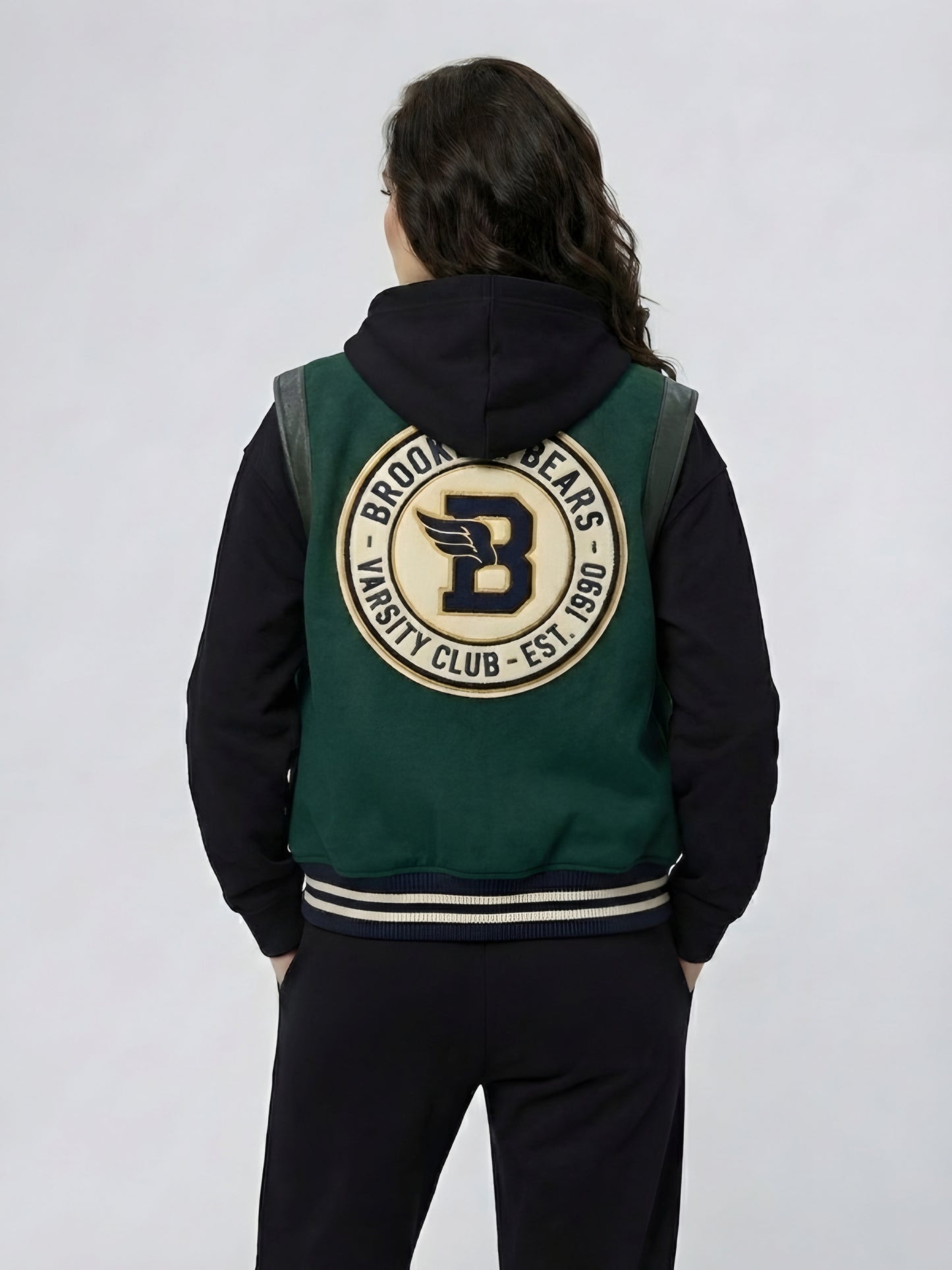 Person wearing a green and black varsity jacket with a logo on the back against a white background