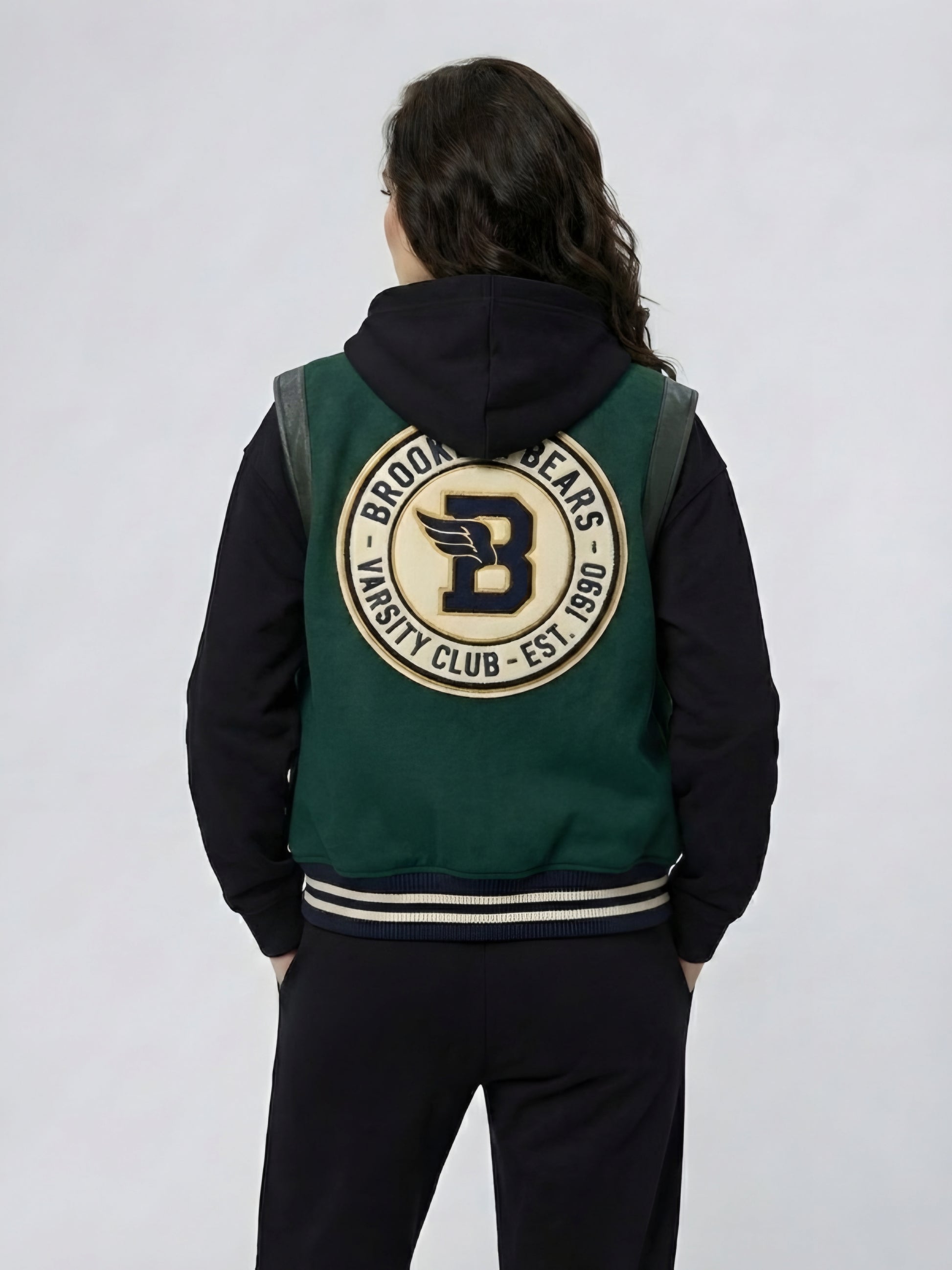 Person wearing a green and black varsity jacket with a logo on the back against a white background
