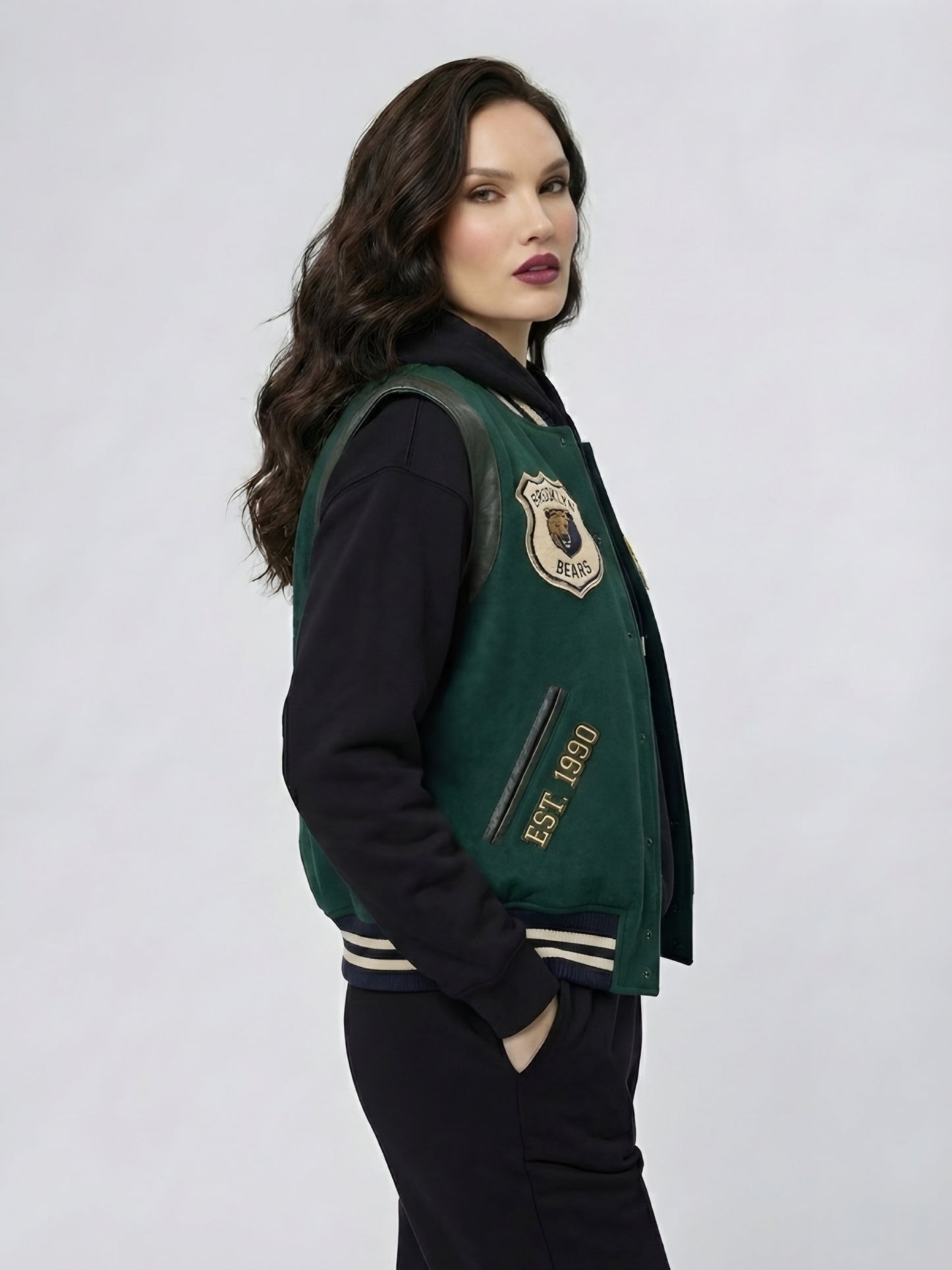 Woman wearing a green varsity jacket with a school emblem on a white background