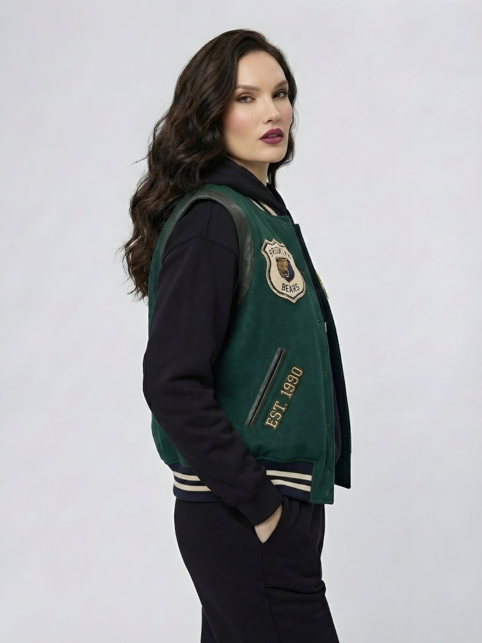 Woman wearing a green varsity jacket with a school emblem on a white background