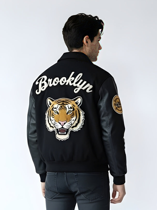Person wearing a black bomber jacket with 'Brooklyn' and a tiger design on the back, against a white background.