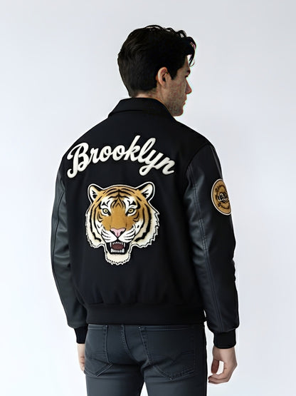 Person wearing a black bomber jacket with 'Brooklyn' and a tiger design on the back, against a white background.