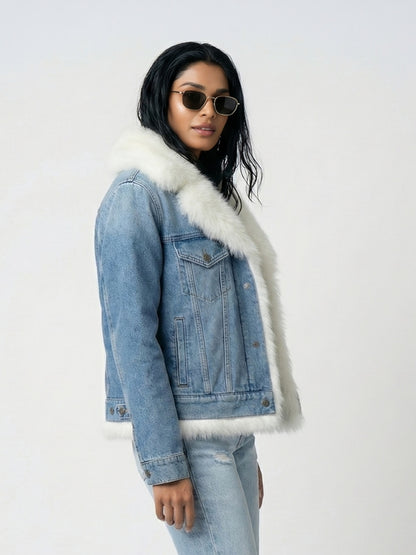 Person wearing a denim jacket with white fur trim on a plain background