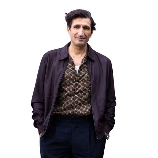 Man wearing a dark jacket over a patterned shirt on a white background