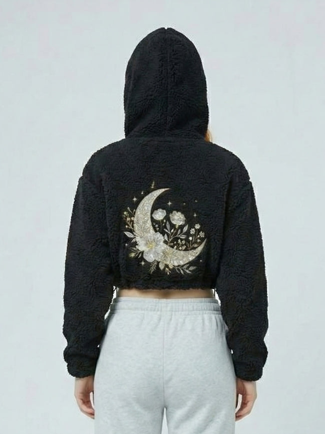 Person wearing a black hoodie with a floral crescent moon design on the back against a light gray background