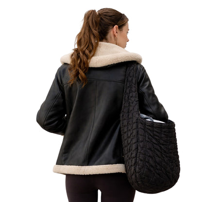 Woman wearing a black leather jacket with beige fur collar holding a textured black bag on a white background