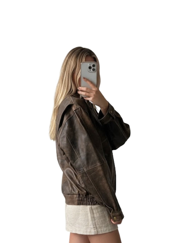 Person wearing a brown jacket taking a mirror selfie on a white background