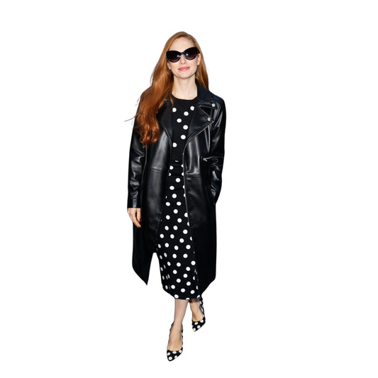 Woman wearing a black leather coat over a black and white polka dot dress on a white background