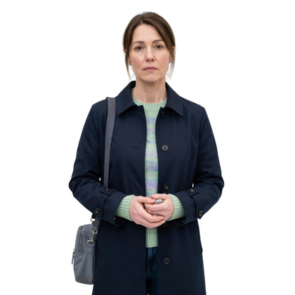 Woman wearing a navy coat and green sweater with a gray bag on a white background