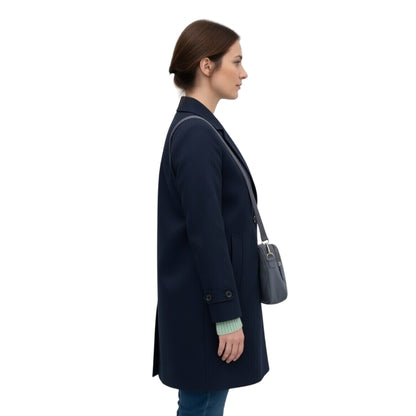 Woman wearing a navy coat holding a gray handbag on a white background
