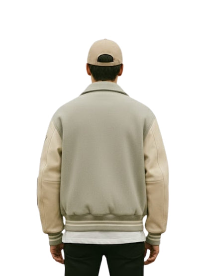 Person wearing a beige varsity jacket with leather sleeves on a white background