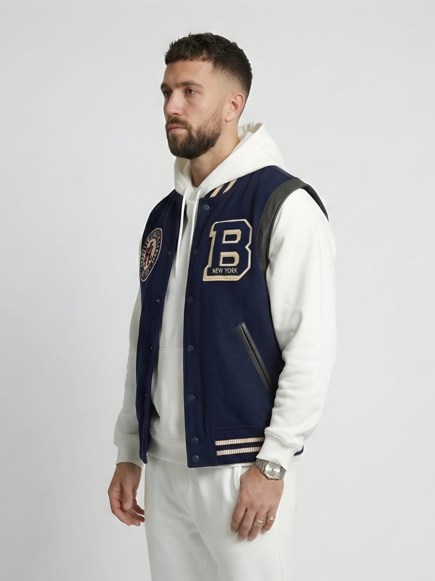Man wearing a navy varsity jacket with a letter 'B' emblem on a white background