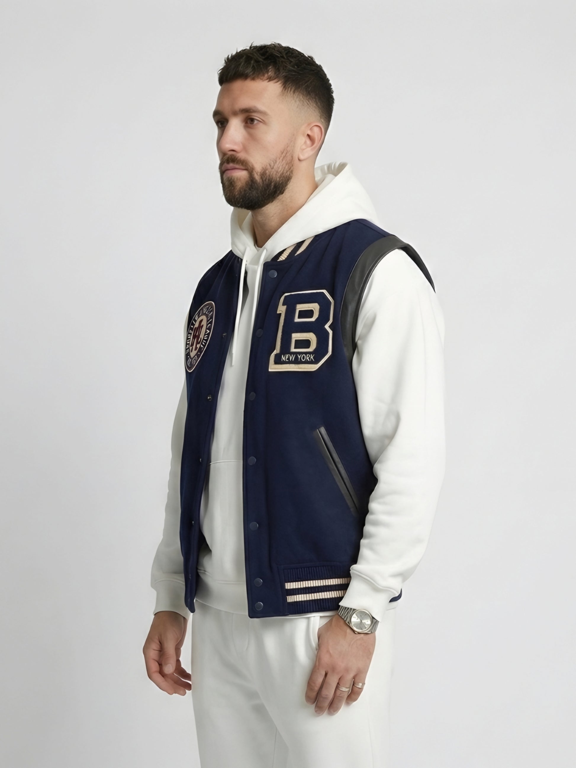 Man wearing a navy varsity jacket with a letter 'B' emblem on a white background
