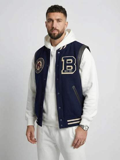 Man wearing a navy varsity jacket with patches on a plain background