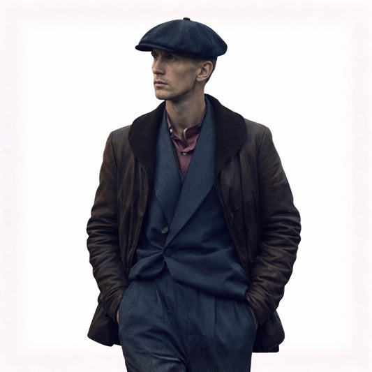 Man wearing a dark coat, gray suit, and flat cap on a white background