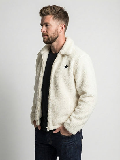 Man wearing a white sherpa jacket with a star design on a plain background
