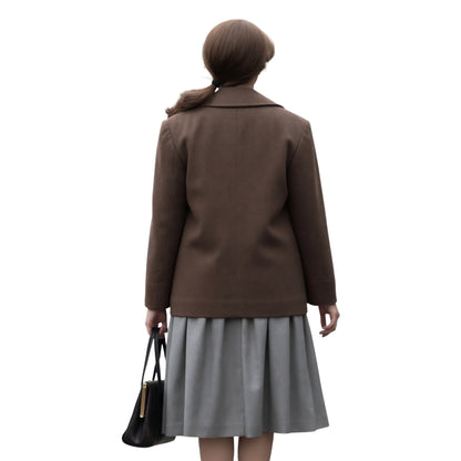 Person wearing a brown coat and gray skirt holding a black handbag on a white background