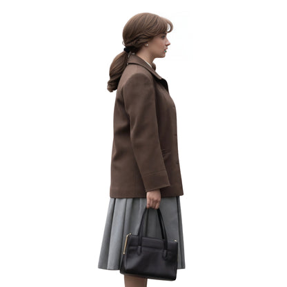 Woman wearing a brown coat and gray skirt holding a black handbag on a white background