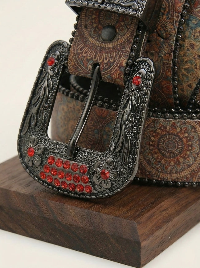 Decorative belt buckle with intricate designs and red stones on a wooden surface.
