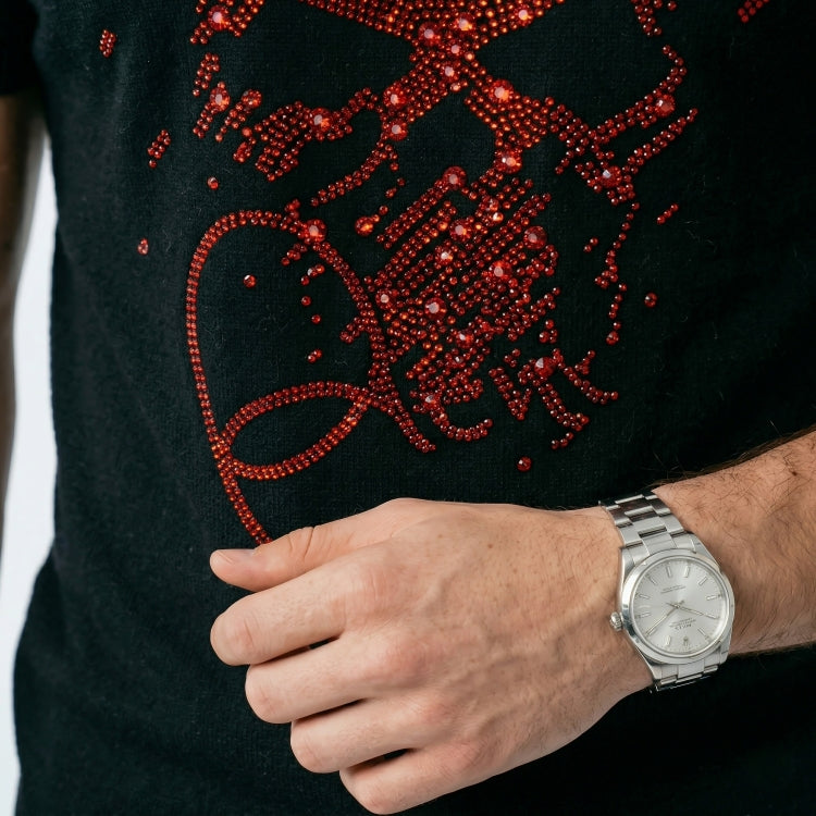 Black garment with red embellishments and a hand wearing a silver watch.