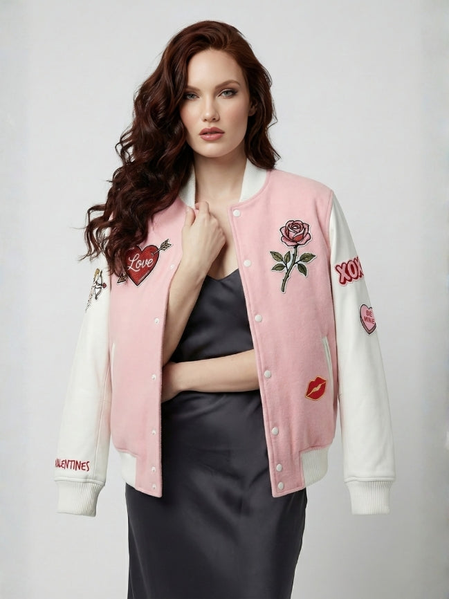 Woman wearing a pink and white varsity jacket with embroidered designs on a plain background