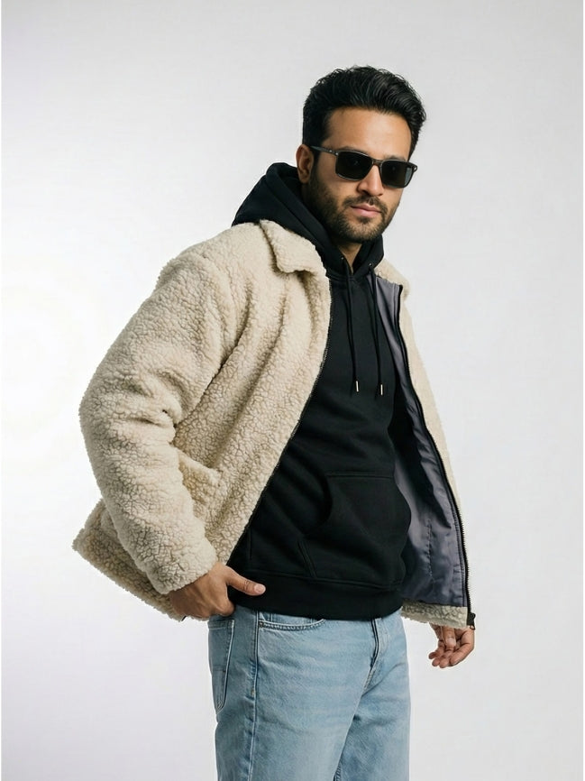Man wearing a beige sherpa jacket over a black hoodie with sunglasses on a white background