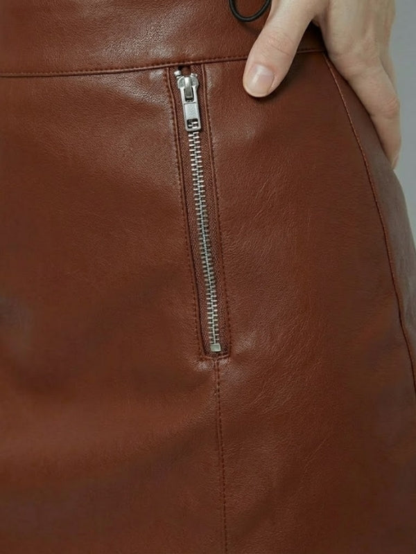 Close-up of a brown leather bag with a zipper, held by a hand.