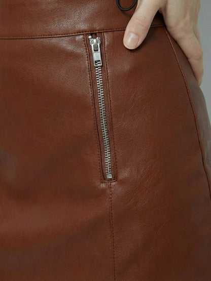 Close-up of a brown leather bag with a zipper, held by a hand.