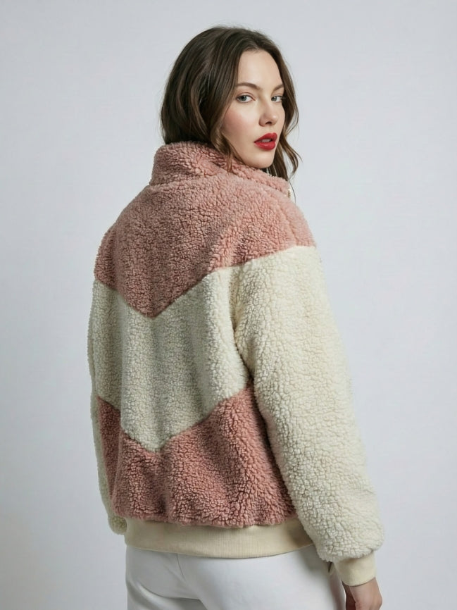 Woman wearing a two-tone sherpa jacket with pink and beige colors on a plain background