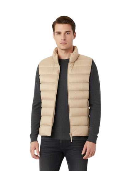 Man wearing a beige puffer vest over a dark long-sleeve shirt on a white background