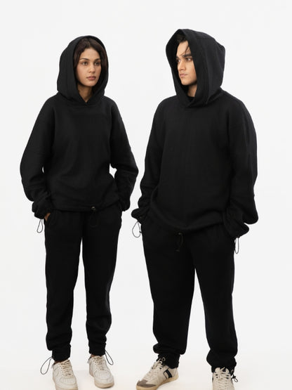 Two people wearing black hoodies and pants on a white background