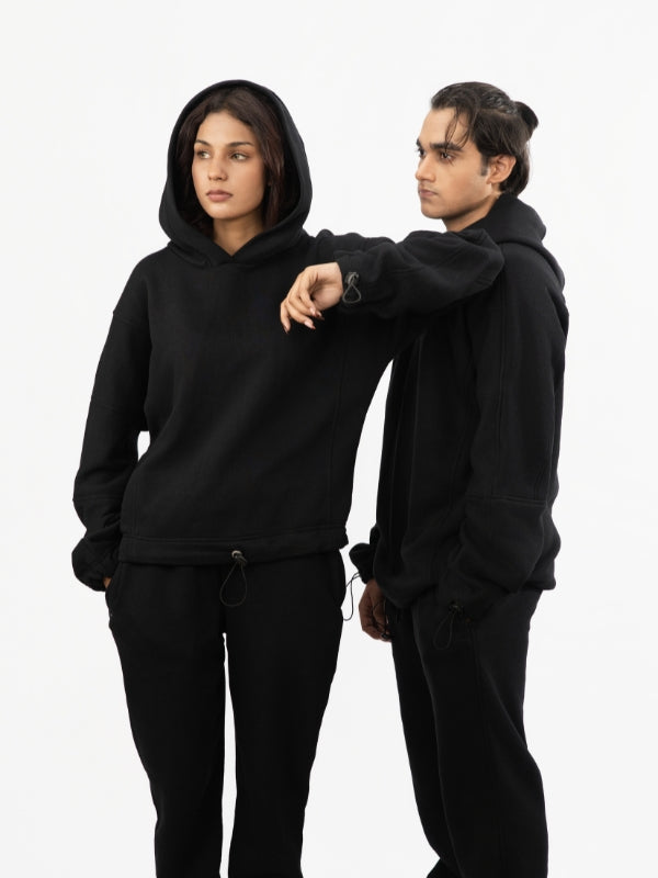 Two people wearing black hoodies and pants on a white background