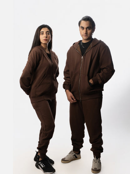 Two people wearing matching brown tracksuits on a white background