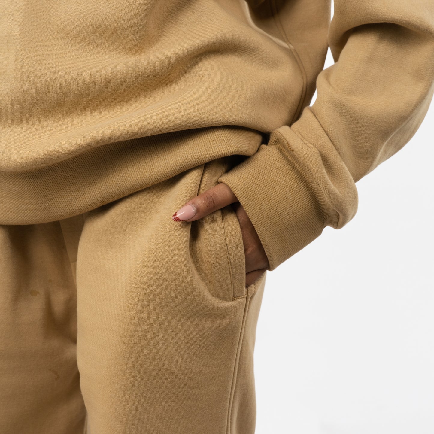 Close-up of a person wearing a beige tracksuit with hands in pockets on a light gray background