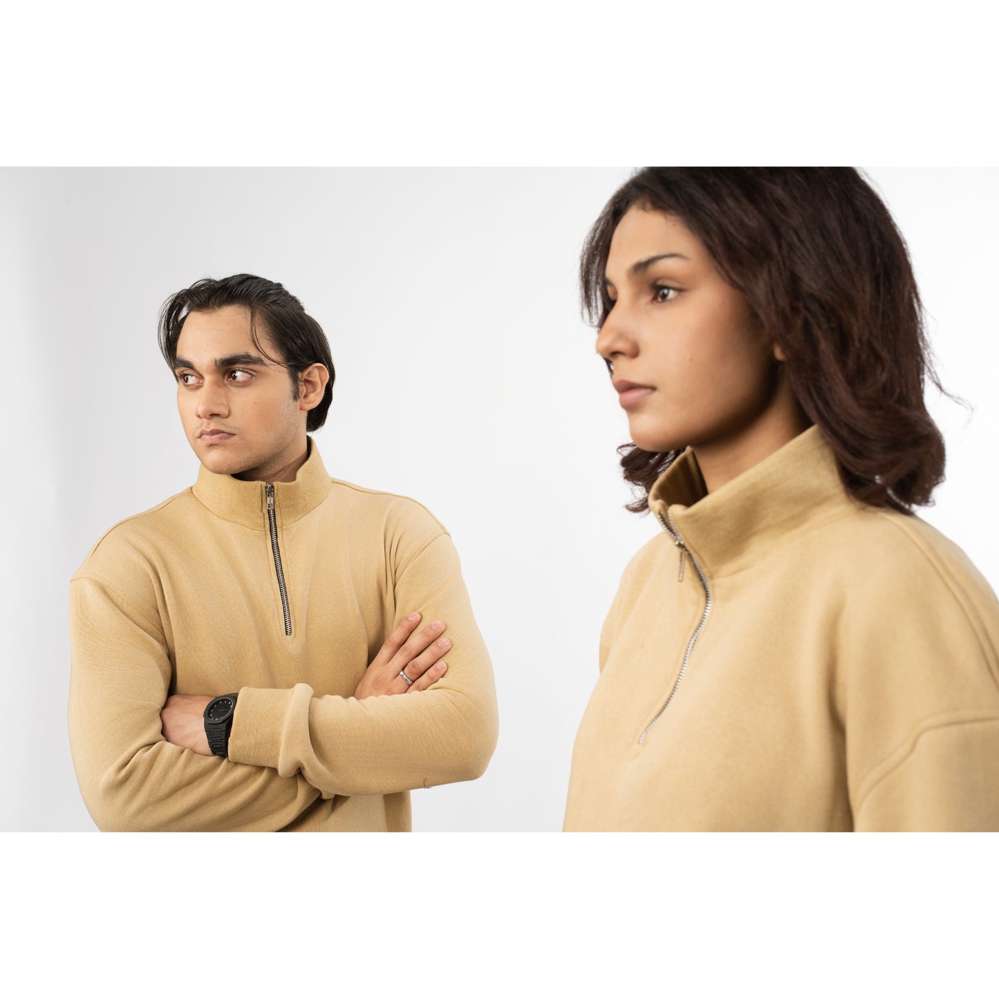 Two people wearing beige half-zip sweatshirts against a white background