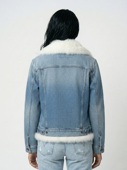 Person wearing a denim jacket with white fur trim on a plain background