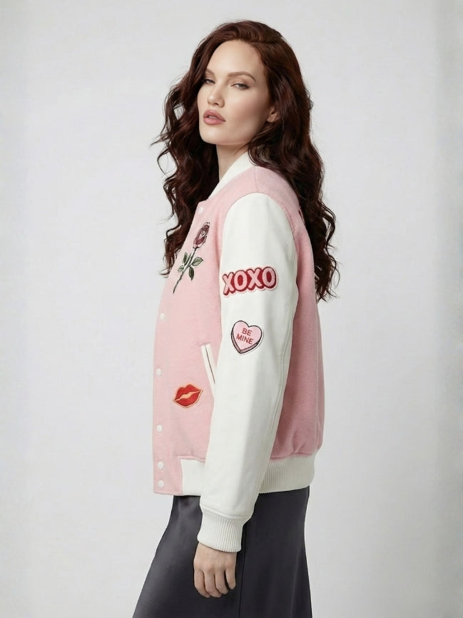 Woman wearing a pink and white varsity jacket with various designs on a plain background