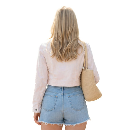 Woman wearing a light pink jacket and denim shorts, holding a beige bag on a white background