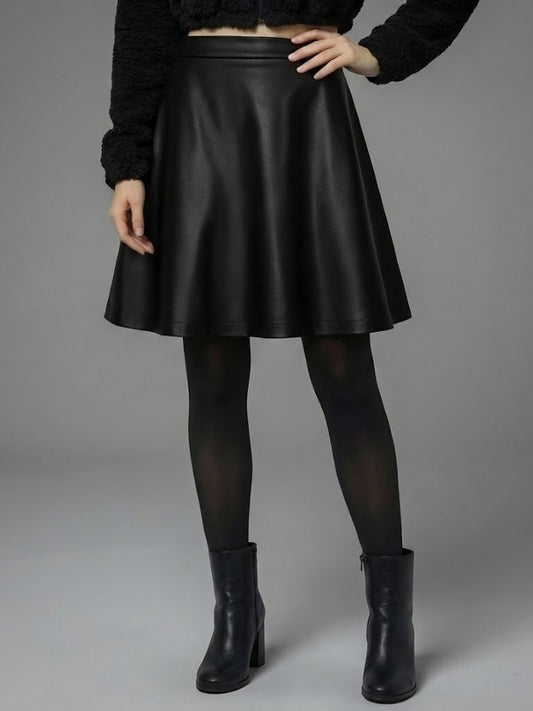 Person wearing a black leather skirt with black tights and boots on a gray background