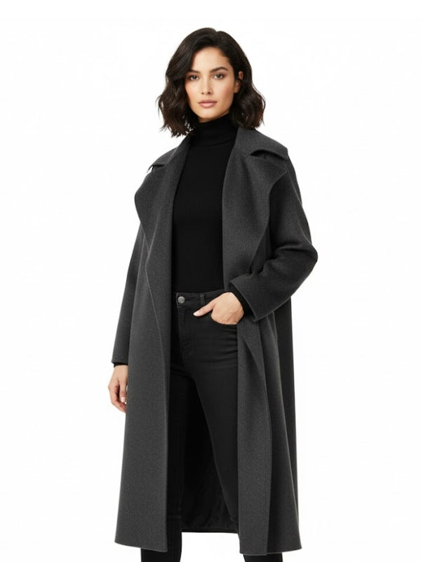 Woman wearing a long dark gray coat over a black outfit on a white background