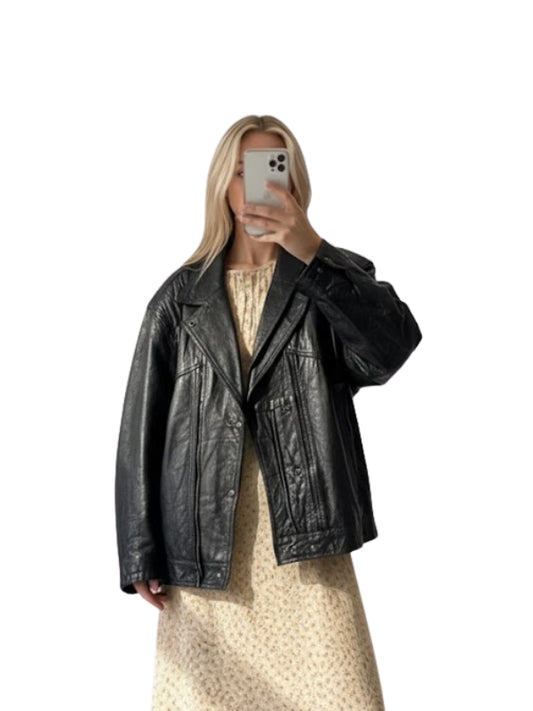 Person wearing a black leather jacket taking a mirror selfie on a white background