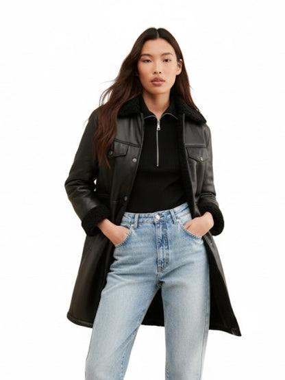 Woman wearing a black leather coat, black top, and light blue jeans on a white background